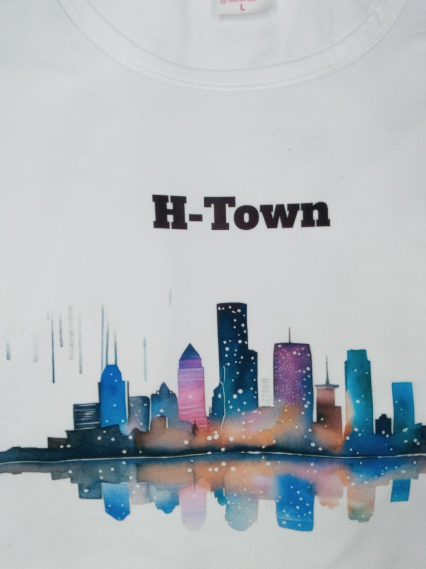 White long sleeve t-shirt with the graphic of the skyline of downtown Houston. The graphic is painted in water color style.